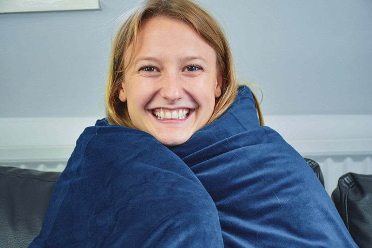 Lachende vrouw gewikkeld in een donkerblauwe verzwaringsdeken op de bank.