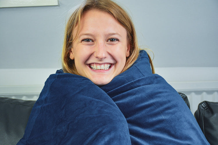 Lachende vrouw gewikkeld in een donkerblauwe verzwaringsdeken in bed.