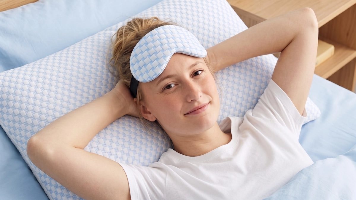 Vrouw ligt ontspannen op haar rug in bed met een slaapmasker op.