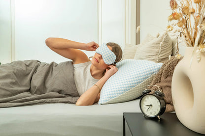 Een vrouw met een slaapmasker houdt haar hand voor haar gezicht, klaar om te ontspannen en te genieten van een goede nachtrust.