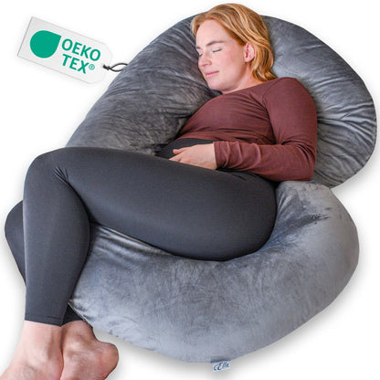 Vrouw ligt op een groot grijs kussen van Ella Sleeps C - Shape Minky, ideaal voor comfort tijdens de zwangerschap.