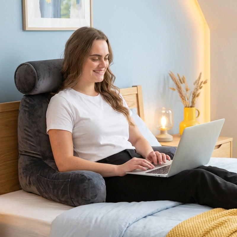 Vrouw werkt met laptop in bed tegen het grijze Ella kussen.