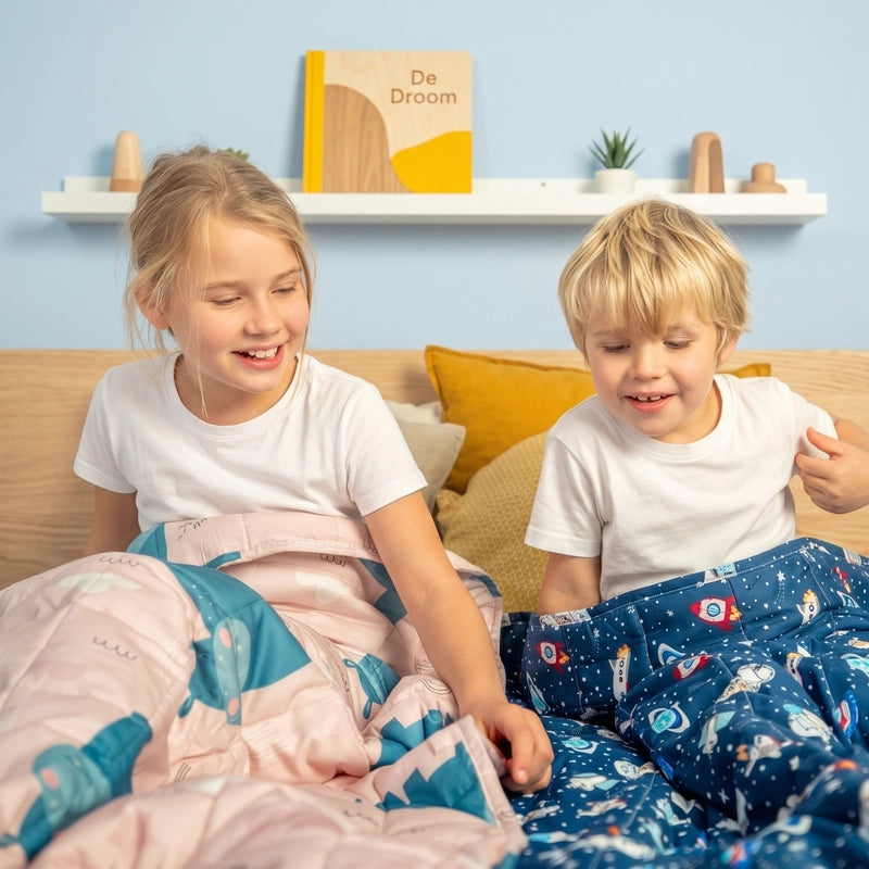 Twee kinderen zitten op bed met een donkerblauwe kinderverzwaringsdeken met print.